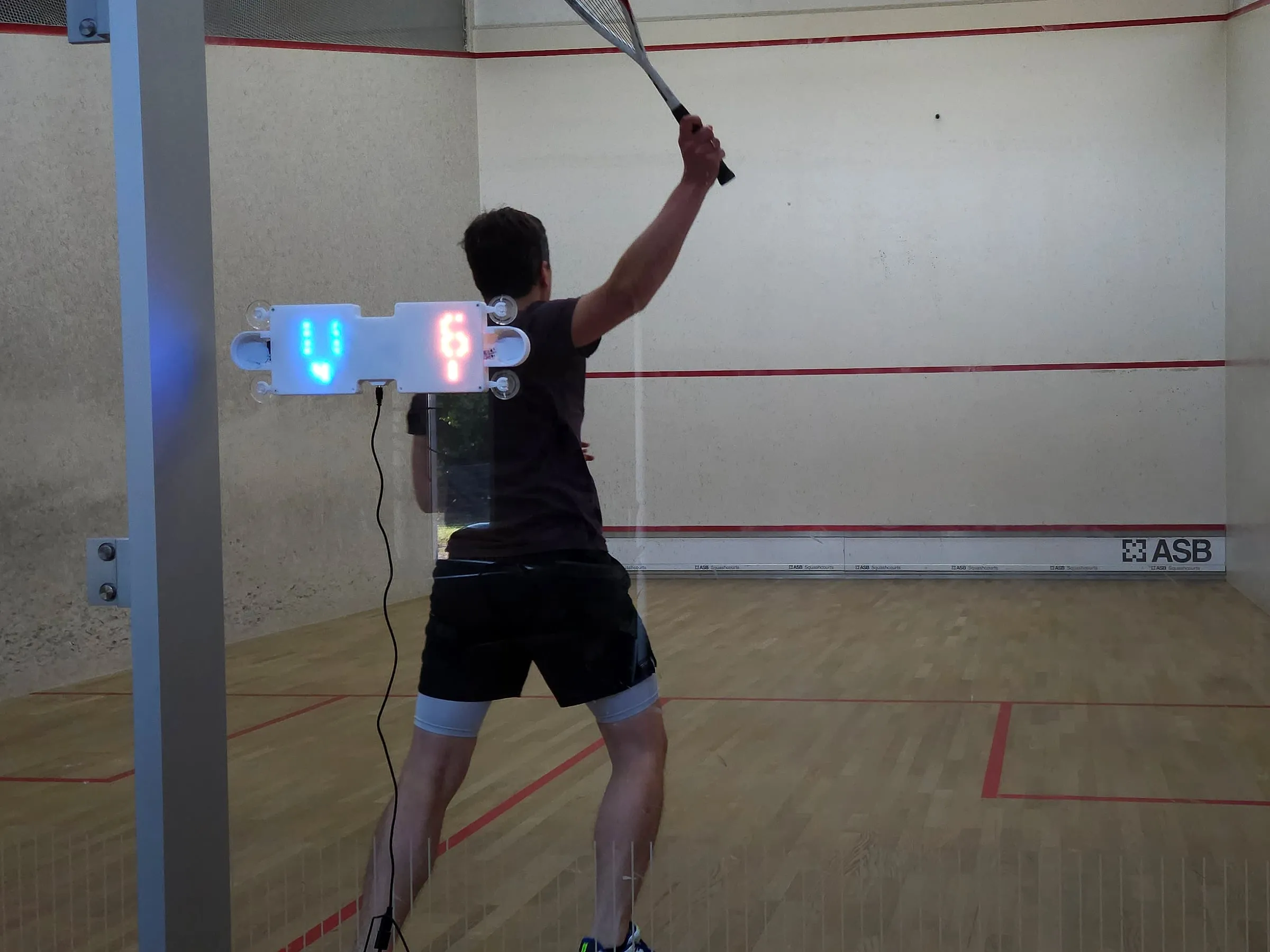 A player mid-shot, with the match score glowing on the glass beside the player